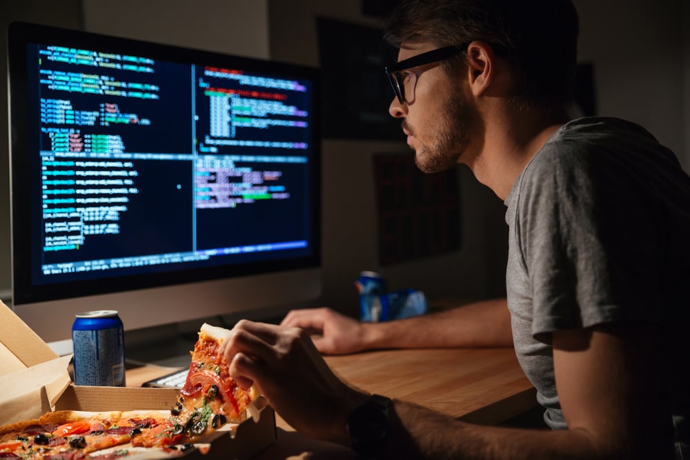 Perfil de um jovem programador de software concentrado a comer pizza e a programar em casa