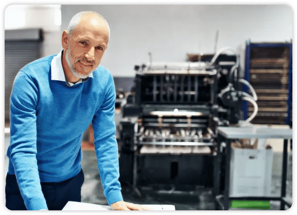 homem mais velho de camisa azul em frente a uma máquina de dobrar papel