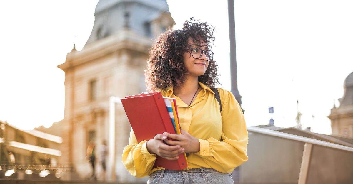 Estudante do sexo feminino com livros na mão em frente ao edifício da faculdade 