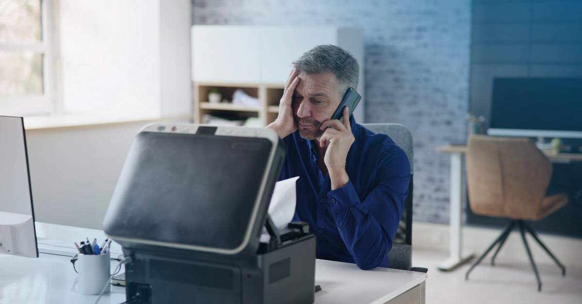 Homem confuso ao telefone a olhar para a impressora